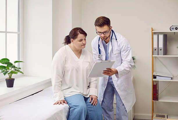 Médico mostrando una gráfica a un paciente durante una consulta de apoyo en un consultorio médico luminoso.