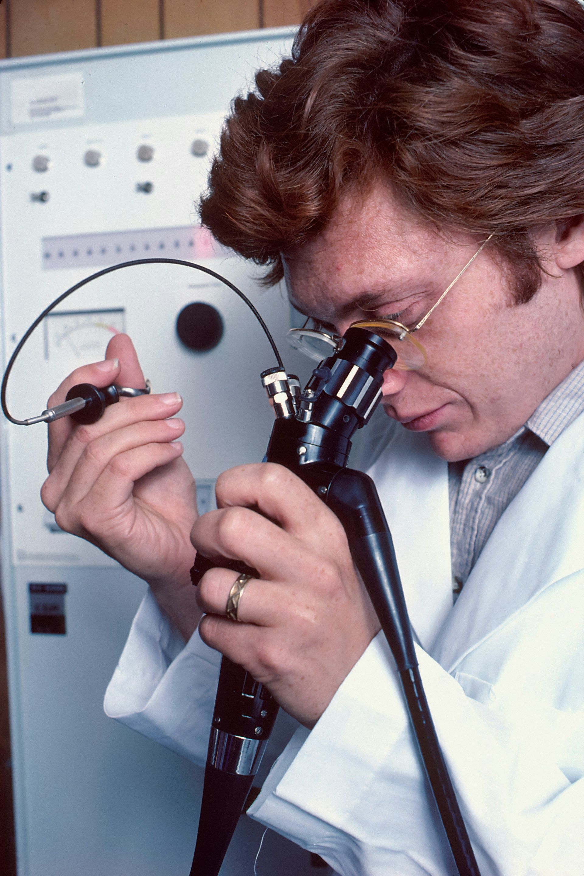 Un médico caucásico utilizando un endoscopio controlado de forma remota. Está mirando a través de un ocular similar a un microscopio para monitorear sus acciones mientras usa pequeños cepillos y cuchillos para tomar una biopsia.