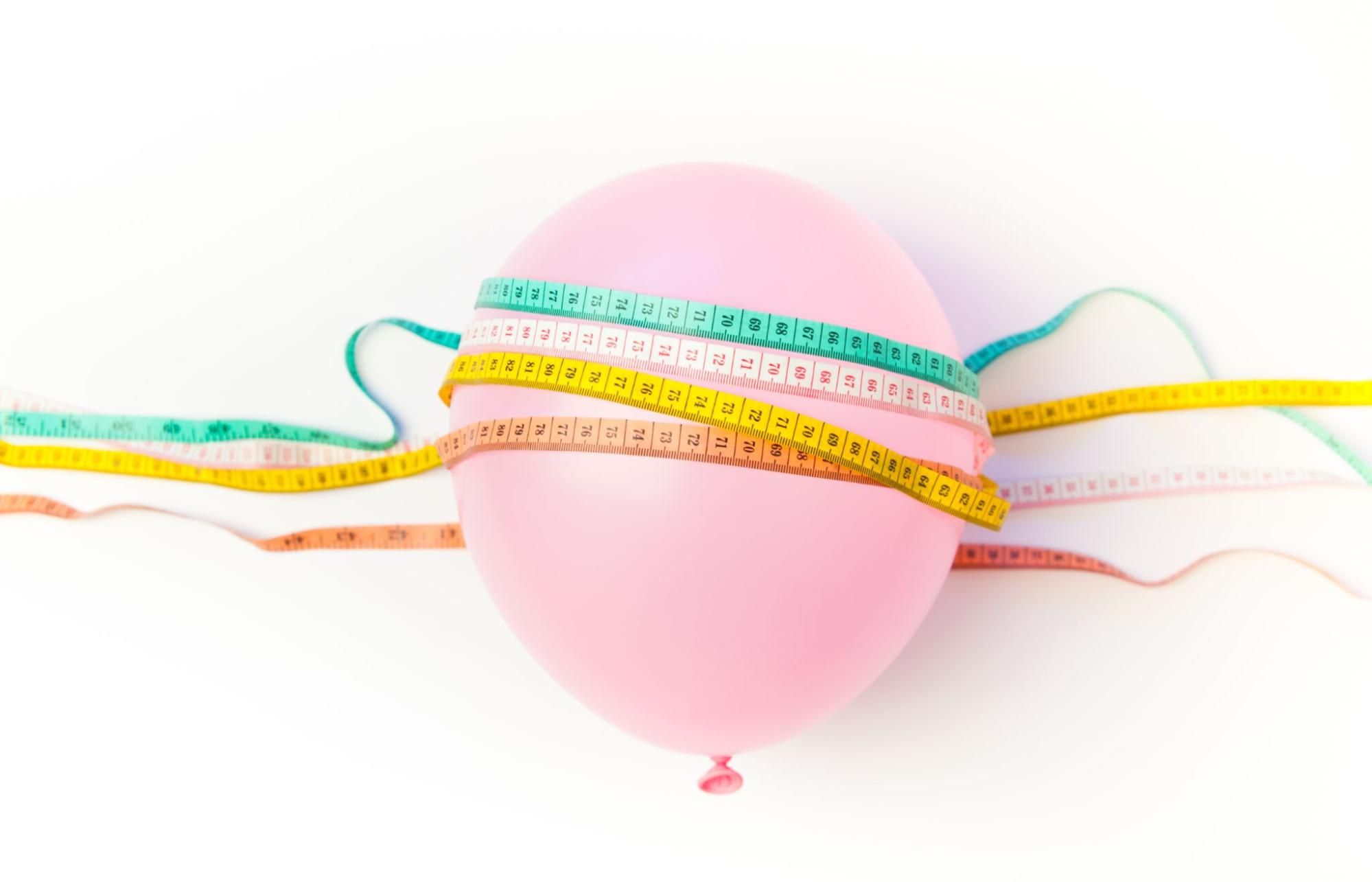 A pink balloon wrapped with multiple measuring tapes, symbolizing weight loss and measurement.
