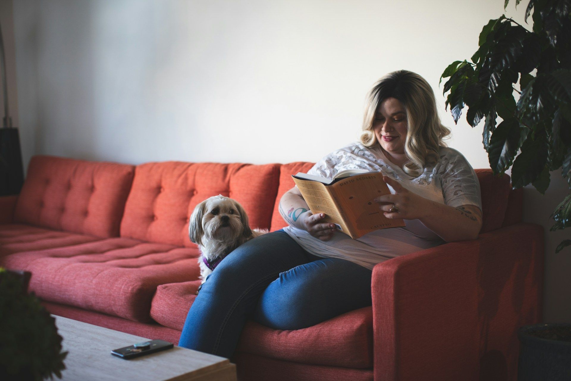 Mujer blanca de talla grande leyendo en el sofá con un perro.